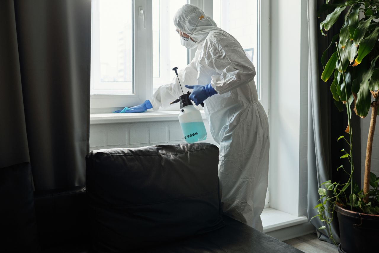 about-us-01 Person in PPE disinfecting indoor window area during COVID-19 pandemic.
